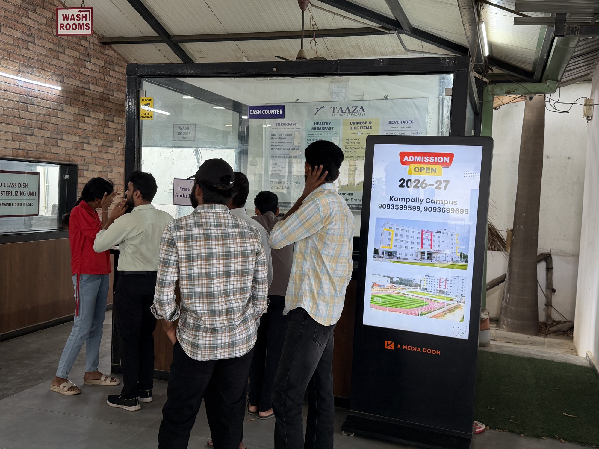 School admissions campaign on K MEDIA DOOH standee at a busy restaurant counter